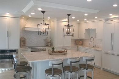 Inspiration for a mid-sized coastal l-shaped light wood floor open concept kitchen remodel in Miami with a drop-in sink, shaker cabinets, white cabinets, marble countertops, white backsplash, stone tile backsplash, paneled appliances and an island