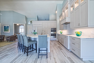Example of a mid-sized transitional porcelain tile eat-in kitchen design in Miami with an undermount sink, shaker cabinets, gray cabinets, quartzite countertops, gray backsplash, stone tile backsplash, paneled appliances and an island