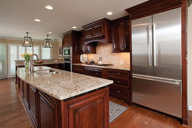 Kitchen - large traditional l-shaped medium tone wood floor kitchen idea in Atlanta with a double-bowl sink, raised-panel cabinets, dark wood cabinets, granite countertops, beige backsplash, stone tile backsplash, stainless steel appliances and an island