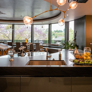 Photo of an expansive contemporary u-shaped eat-in kitchen in Los Angeles with an undermount sink, flat-panel cabinets, grey cabinets, granite benchtops, black splashback, stone slab splashback, stainless steel appliances, multiple islands, black benchtop, porcelain floors and yellow floor.