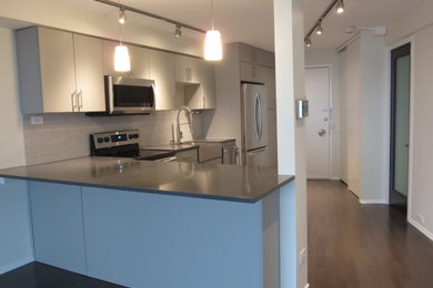 Photo of a medium sized contemporary single-wall open plan kitchen in Chicago with a belfast sink, flat-panel cabinets, grey cabinets, engineered stone countertops, grey splashback, porcelain splashback, stainless steel appliances, medium hardwood flooring, a breakfast bar, brown floors and grey worktops.