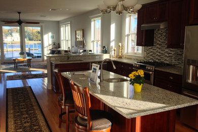 Kitchen - medium tone wood floor kitchen idea in Boston with raised-panel cabinets, granite countertops, glass tile backsplash, stainless steel appliances, an island, an undermount sink and dark wood cabinets