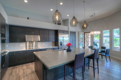 Inspiration for a mid-sized modern l-shaped eat-in kitchen remodel in Phoenix with flat-panel cabinets, dark wood cabinets, gray backsplash, stainless steel appliances and an island
