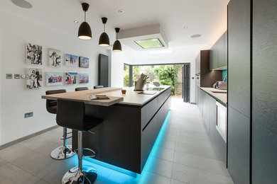 Example of a large trendy single-wall ceramic tile and gray floor eat-in kitchen design in Buckinghamshire with an undermount sink, flat-panel cabinets, black cabinets, quartz countertops, blue backsplash, glass sheet backsplash, paneled appliances and an island