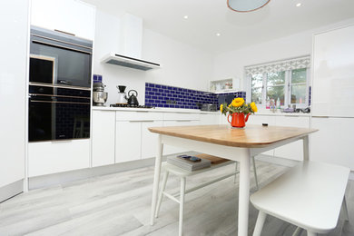 This is an example of a medium sized contemporary u-shaped enclosed kitchen in Other with an integrated sink, flat-panel cabinets, white cabinets, composite countertops, blue splashback, ceramic splashback, black appliances and white worktops.
