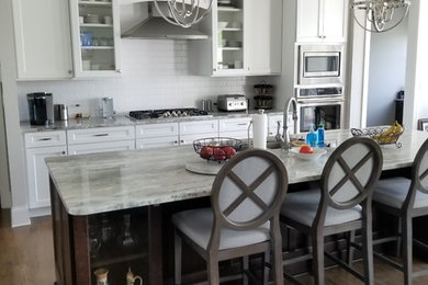 Example of a large transitional galley medium tone wood floor and brown floor kitchen design in Charlotte with an undermount sink, recessed-panel cabinets, white cabinets, quartzite countertops, white backsplash, subway tile backsplash, an island and white countertops
