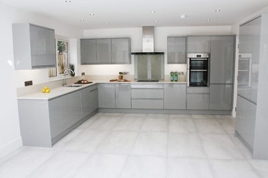 Moderne Küche in L-Form mit integriertem Waschbecken, flächenbündigen Schrankfronten, grauen Schränken, Mineralwerkstoff-Arbeitsplatte, Küchengeräten aus Edelstahl und Kalkstein in Belfast