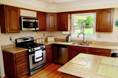 Example of a mid-sized minimalist l-shaped light wood floor eat-in kitchen design in Philadelphia with a double-bowl sink, raised-panel cabinets, brown cabinets, marble countertops, stainless steel appliances and an island