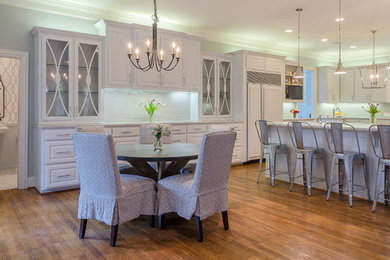 Open concept kitchen - traditional u-shaped medium tone wood floor open concept kitchen idea in Dallas with a farmhouse sink, raised-panel cabinets, white cabinets, marble countertops, beige backsplash, subway tile backsplash, stainless steel appliances and an island