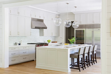 Beach style l-shaped medium tone wood floor and brown floor kitchen photo in Charleston with an undermount sink, shaker cabinets, white cabinets, white backsplash, stainless steel appliances and an island