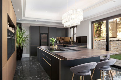 This is an example of a medium sized modern open plan kitchen in Other with flat-panel cabinets, black cabinets, mirror splashback, integrated appliances, an island and black worktops.