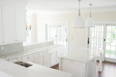 Klassisk inredning av ett kök, med en dubbel diskho, luckor med infälld panel, vita skåp, flerfärgad stänkskydd, stänkskydd i glaskakel, rostfria vitvaror, mellanmörkt trägolv och en köksö