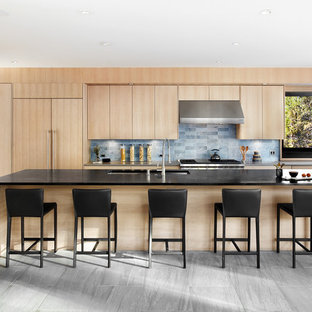Imagen de cocina de galera, contemporánea, abierta, con fregadero bajoencimera, armarios con paneles lisos, puertas de armario de madera clara, encimera de esteatita, salpicadero azul, salpicadero de azulejos de piedra, electrodomésticos con paneles, suelo de baldosas de porcelana y una isla