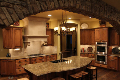 Bild på ett mellanstort vintage kök, med en dubbel diskho, luckor med upphöjd panel, skåp i mörkt trä, granitbänkskiva, beige stänkskydd, stänkskydd i keramik, rostfria vitvaror, mörkt trägolv, en köksö och brunt golv