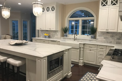 Large elegant l-shaped dark wood floor and brown floor eat-in kitchen photo in Other with a farmhouse sink, quartz countertops, marble backsplash, stainless steel appliances, a peninsula, raised-panel cabinets, white cabinets and gray backsplash