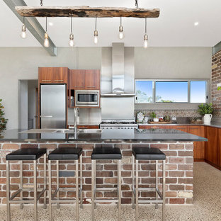 Photo of a midcentury l-shaped kitchen in Brisbane with a triple-bowl sink, flat-panel cabinets, medium wood cabinets, stainless steel benchtops, metallic splashback, stainless steel appliances, terrazzo floors and with island.