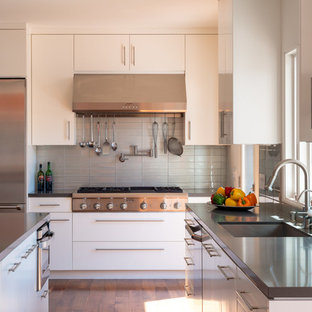 Contemporary kitchen designs - Example of a trendy l-shaped medium tone wood floor kitchen design in Los Angeles with gray backsplash, an island, a single-bowl sink, flat-panel cabinets, white cabinets, solid surface countertops, glass tile backsplash and stainless steel appliances