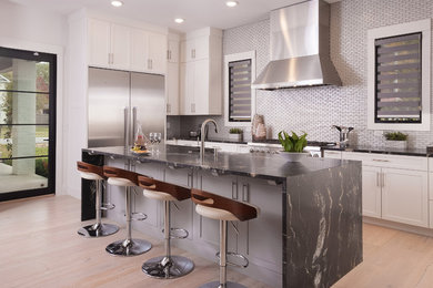 Transitional l-shaped light wood floor and beige floor kitchen photo in Other with shaker cabinets, white cabinets, metallic backsplash, metal backsplash, stainless steel appliances, an island and black countertops