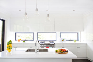 Cette image montre une cuisine ouverte parallèle design de taille moyenne avec un évier 2 bacs, des portes de placard blanches, une crédence blanche, un électroménager en acier inoxydable et îlot.