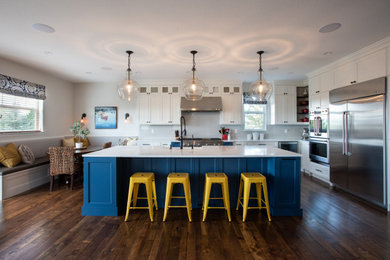 Eat-in kitchen - large traditional l-shaped medium tone wood floor and brown floor eat-in kitchen idea in Denver with a farmhouse sink, shaker cabinets, blue cabinets, solid surface countertops, white backsplash, subway tile backsplash, stainless steel appliances, an island and white countertops