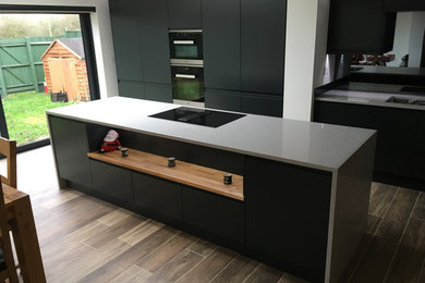 This is an example of a modern single-wall kitchen/diner in Oxfordshire with an integrated sink, flat-panel cabinets, black cabinets, quartz worktops, mirror splashback, integrated appliances and an island.