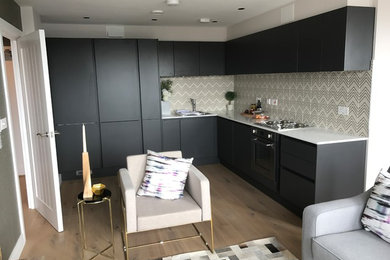 This is an example of a medium sized modern l-shaped open plan kitchen in Dorset with a built-in sink, flat-panel cabinets, black cabinets, quartz worktops and integrated appliances.