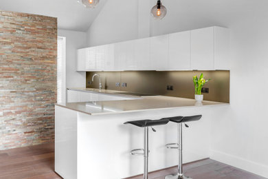 This is an example of a large contemporary l-shaped kitchen/diner in Other with a submerged sink, flat-panel cabinets, white cabinets, composite countertops, metallic splashback, mirror splashback, laminate floors, a breakfast bar, brown floors and beige worktops.