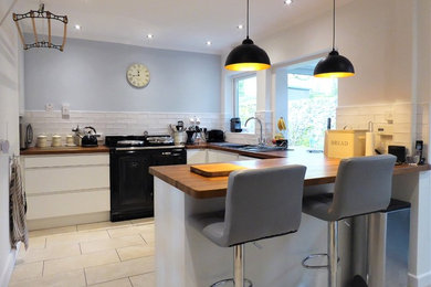 Small contemporary u-shaped enclosed kitchen in Other with a single-bowl sink, flat-panel cabinets, white cabinets, wood worktops, metro tiled splashback, limestone flooring, a breakfast bar, beige floors and brown worktops.
