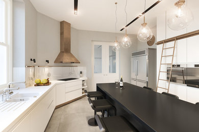 Photo of a contemporary enclosed kitchen in London with a double-bowl sink, flat-panel cabinets, white splashback, glass sheet splashback, stainless steel appliances, concrete flooring, an island, grey floors and white worktops.