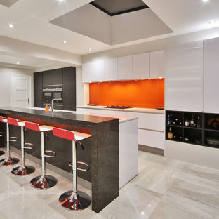 This is an example of a medium sized contemporary galley kitchen in London with a submerged sink, flat-panel cabinets, white cabinets, quartz worktops, orange splashback, glass sheet splashback, black appliances, porcelain flooring, an island, beige floors and white worktops.