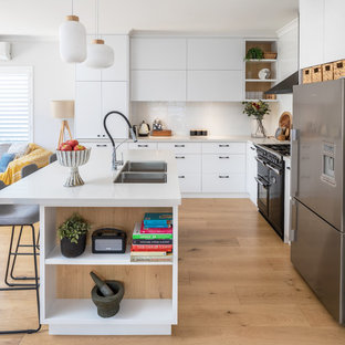 This is an example of a modern kitchen in Perth with flat-panel cabinets, white cabinets, quartz benchtops, white splashback, subway tile splashback, medium hardwood floors, with island, white benchtop, a double-bowl sink, stainless steel appliances and brown floor.