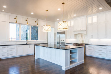 Example of a large transitional galley medium tone wood floor and brown floor eat-in kitchen design in Dallas with a drop-in sink, recessed-panel cabinets, white cabinets, granite countertops, white backsplash, ceramic backsplash, stainless steel appliances, an island and black countertops