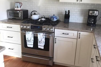 Mid-sized farmhouse u-shaped medium tone wood floor and brown floor enclosed kitchen photo in New York with an undermount sink, shaker cabinets, white cabinets, granite countertops, white backsplash, subway tile backsplash, stainless steel appliances and an island