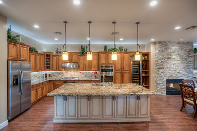 Example of a huge classic l-shaped porcelain tile eat-in kitchen design in Phoenix with an undermount sink, raised-panel cabinets, beige cabinets, granite countertops, brown backsplash, stone tile backsplash, stainless steel appliances and an island