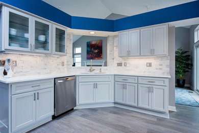 Photo of a medium sized modern u-shaped open plan kitchen in Columbus with a double-bowl sink, shaker cabinets, white cabinets, engineered stone countertops, white splashback, marble splashback, stainless steel appliances, medium hardwood flooring, no island, brown floors and white worktops.