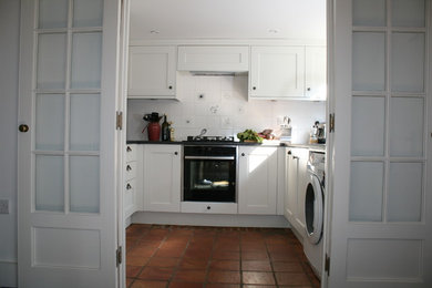 Exempel på ett avskilt, litet klassiskt svart svart u-kök, med en enkel diskho, skåp i shakerstil, vita skåp, granitbänkskiva, vitt stänkskydd, stänkskydd i keramik, integrerade vitvaror, klinkergolv i terrakotta och brunt golv