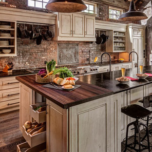 Large country l-shaped open plan kitchen in Denver with raised-panel cabinets, panelled appliances, dark hardwood floors, with island, an integrated sink, beige cabinets, red splashback, brick splashback, brown floor and black benchtop.