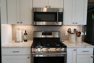 Ejemplo de cocina de estilo americano con armarios estilo shaker, puertas de armario blancas, encimera de cuarcita, salpicadero verde, electrodomésticos de acero inoxidable y suelo marrón