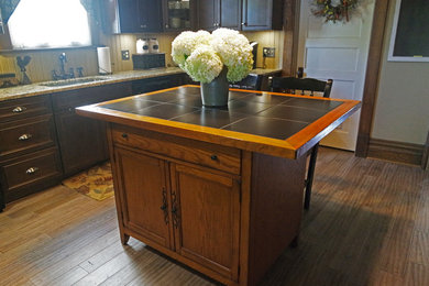 Example of a mid-sized classic u-shaped light wood floor eat-in kitchen design in Other with a single-bowl sink, beaded inset cabinets, dark wood cabinets, granite countertops, beige backsplash, stone tile backsplash, black appliances and an island