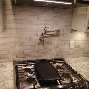 Cette image montre une grand cuisine ouverte traditionnelle en L avec un évier de ferme, un placard avec porte à panneau encastré, des portes de placard en bois vieilli, un plan de travail en quartz modifié, une crédence grise, une crédence en carrelage de pierre, un électroménager en acier inoxydable, un sol en bois foncé, un îlot central, un sol marron et un plan de travail blanc.
