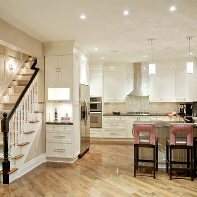 Large transitional u-shaped light wood floor kitchen photo in Toronto with recessed-panel cabinets, white cabinets, beige backsplash, stainless steel appliances, stone tile backsplash and quartz countertops