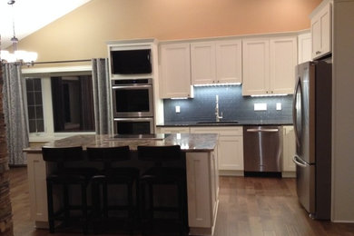 Mid-sized trendy l-shaped medium tone wood floor eat-in kitchen photo in Wichita with an undermount sink, shaker cabinets, white cabinets, granite countertops, black backsplash, stainless steel appliances and an island