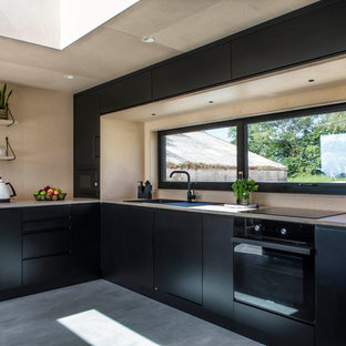 This is an example of a scandinavian l-shaped kitchen in Oxfordshire with a built-in sink, flat-panel cabinets, black cabinets, wood worktops, window splashback, black appliances, concrete flooring, grey floors and beige worktops.