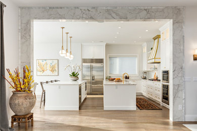 Example of a trendy l-shaped light wood floor and beige floor kitchen design in Calgary with an undermount sink, shaker cabinets, white cabinets, quartz countertops, white backsplash, mosaic tile backsplash, stainless steel appliances, two islands and white countertops