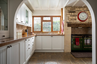 Immagine di una cucina a L country chiusa e di medie dimensioni con lavello da incasso, ante in stile shaker, ante bianche, top in granito, pavimento in pietra calcarea e travi a vista