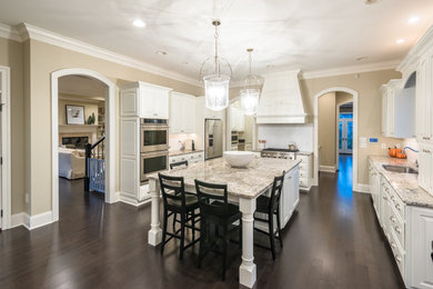 Example of a large transitional u-shaped dark wood floor and brown floor eat-in kitchen design in Other with an island, a drop-in sink, raised-panel cabinets, white cabinets, granite countertops, white backsplash, subway tile backsplash and stainless steel appliances