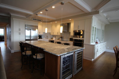 This is an example of a large traditional l-shaped kitchen/diner in Miami with a submerged sink, shaker cabinets, white cabinets, engineered stone countertops, beige splashback, mosaic tiled splashback, stainless steel appliances, medium hardwood flooring, an island and brown floors.