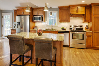 Exempel på ett stort klassiskt kök, med en dubbel diskho, luckor med infälld panel, skåp i mellenmörkt trä, granitbänkskiva, stänkskydd i keramik, rostfria vitvaror, ljust trägolv och en köksö
