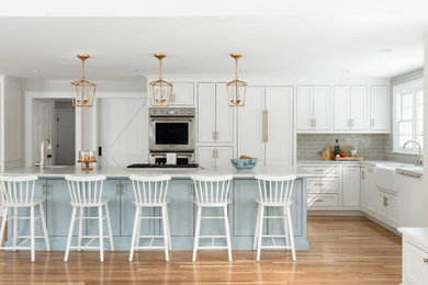 Open concept kitchen - large transitional l-shaped light wood floor and beige floor open concept kitchen idea in Boston with a farmhouse sink, shaker cabinets, white cabinets, quartzite countertops, gray backsplash, subway tile backsplash, paneled appliances, an island and white countertops