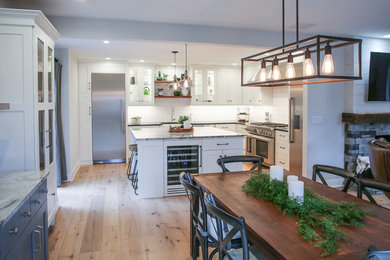 Example of a transitional l-shaped light wood floor eat-in kitchen design in Philadelphia with a farmhouse sink, shaker cabinets, white cabinets, granite countertops, white backsplash, ceramic backsplash, stainless steel appliances, an island and black countertops